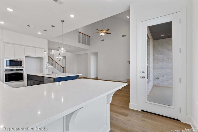 kitchen featuring pendant lighting, a breakfast bar area, appliances with stainless steel finishes, white cabinetry, and a center island with sink