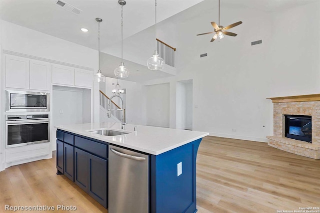 kitchen featuring a stone fireplace, sink, an island with sink, stainless steel appliances, and white cabinets