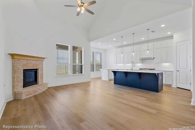 kitchen with pendant lighting, high vaulted ceiling, white cabinetry, an island with sink, and backsplash