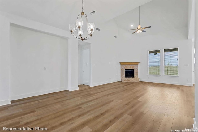 unfurnished living room with ceiling fan with notable chandelier, a stone fireplace, high vaulted ceiling, and hardwood / wood-style flooring