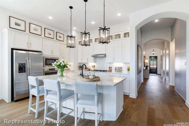 kitchen featuring light stone countertops, hardwood / wood-style floors, a kitchen island with sink, white cabinets, and appliances with stainless steel finishes