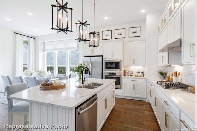 kitchen with sink, light stone counters, a chandelier, a kitchen island with sink, and appliances with stainless steel finishes