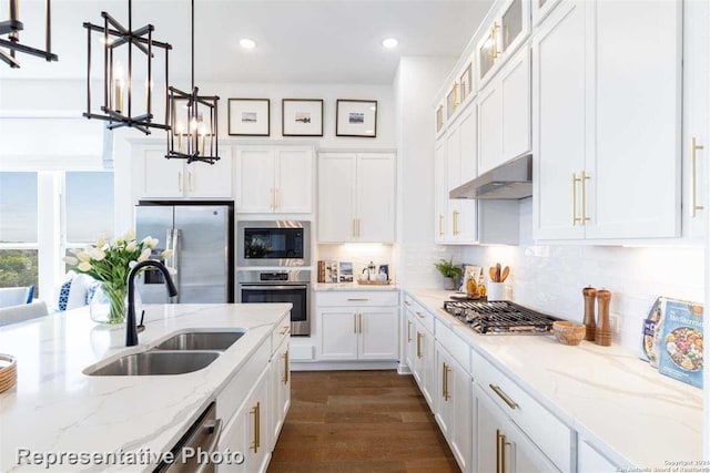 kitchen featuring light stone counters, sink, stainless steel appliances, and hanging light fixtures