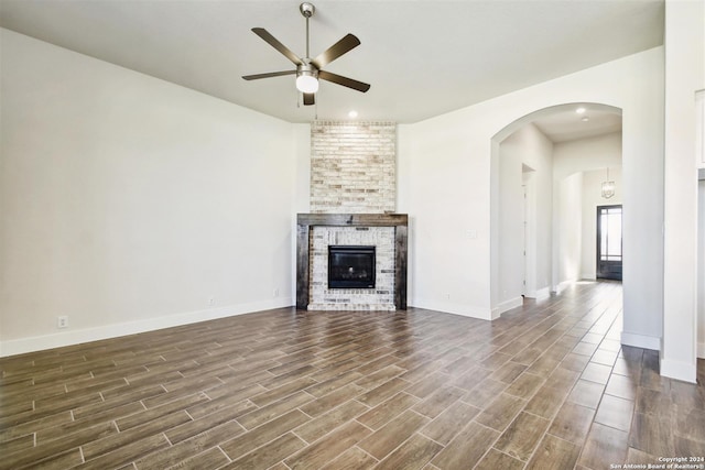 unfurnished living room featuring ceiling fan, a large fireplace, and dark wood-type flooring