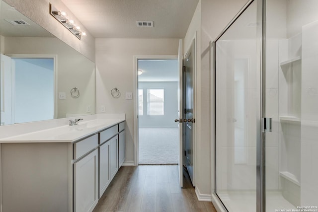 bathroom featuring hardwood / wood-style flooring, vanity, a shower with door, and a textured ceiling