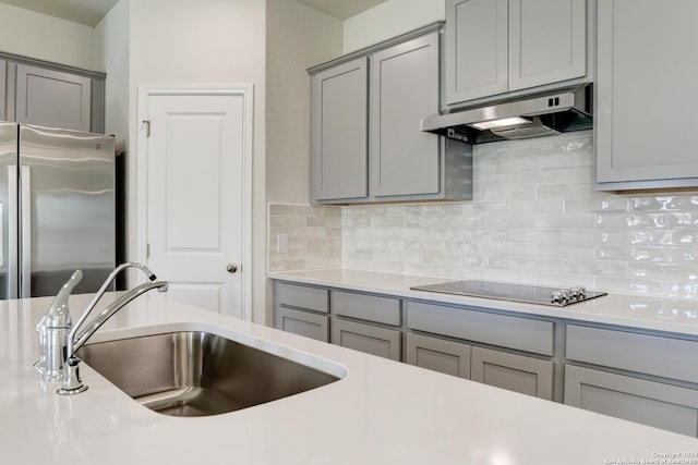 kitchen featuring gray cabinetry, backsplash, black electric stovetop, sink, and stainless steel refrigerator