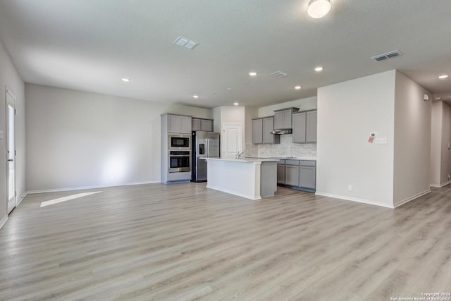 kitchen with decorative backsplash, appliances with stainless steel finishes, light wood-type flooring, gray cabinetry, and a center island with sink