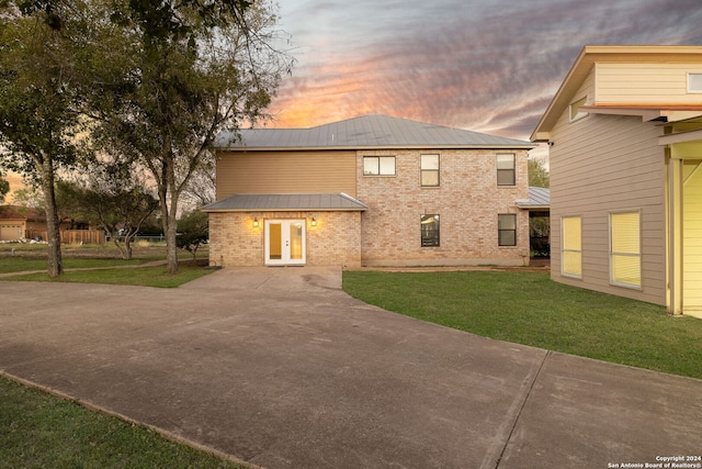 back house at dusk featuring french doors and a yard