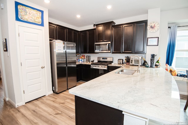 kitchen with kitchen peninsula, appliances with stainless steel finishes, light wood-type flooring, and light stone counters