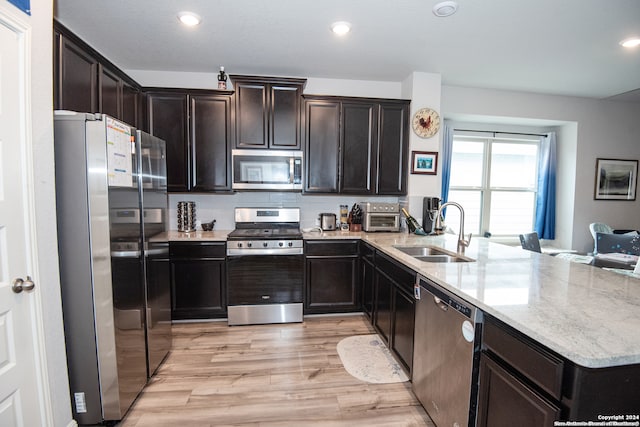 kitchen featuring sink, stainless steel appliances, light stone counters, light hardwood / wood-style flooring, and kitchen peninsula