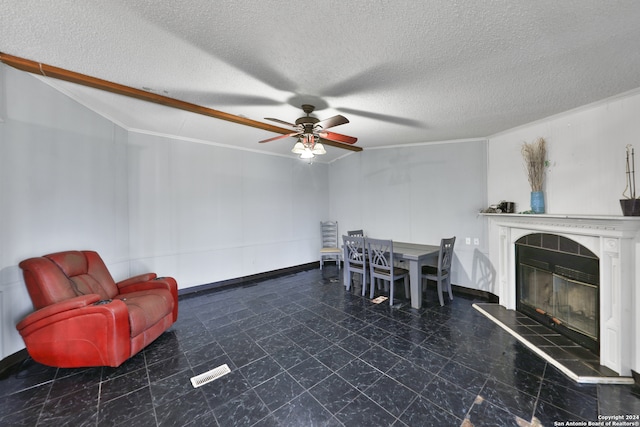 living room with crown molding, vaulted ceiling, ceiling fan, a textured ceiling, and a tiled fireplace