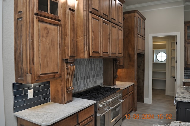 kitchen featuring range with two ovens, crown molding, tasteful backsplash, light hardwood / wood-style floors, and light stone counters