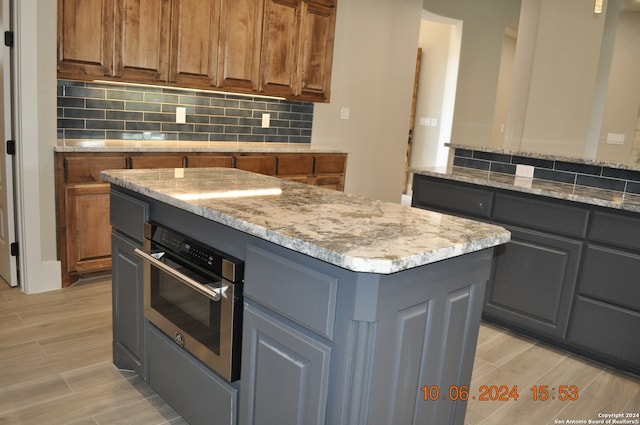 kitchen with light stone countertops, tasteful backsplash, gray cabinetry, a kitchen island, and oven