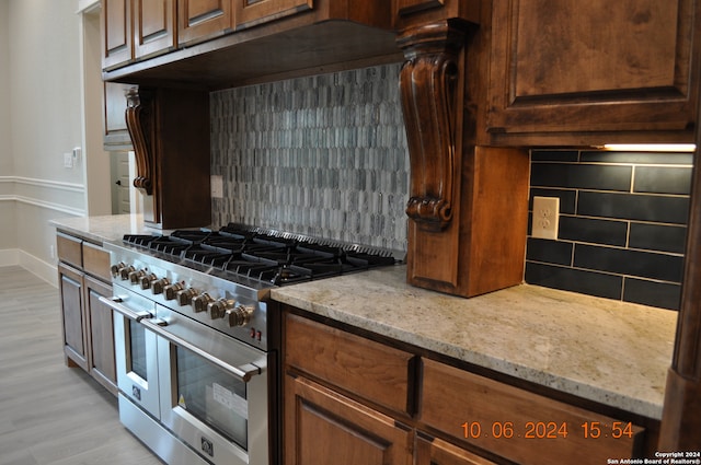 kitchen with light stone counters, light hardwood / wood-style floors, range with two ovens, and backsplash