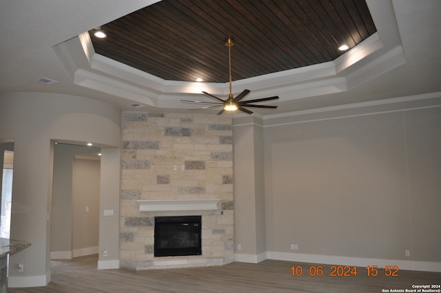 unfurnished living room with a raised ceiling, ceiling fan, ornamental molding, and a stone fireplace