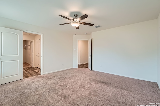 unfurnished bedroom with a walk in closet, a closet, dark carpet, and ceiling fan