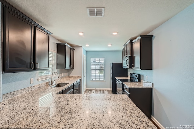 kitchen with light stone countertops, dark brown cabinets, stainless steel appliances, sink, and hardwood / wood-style floors