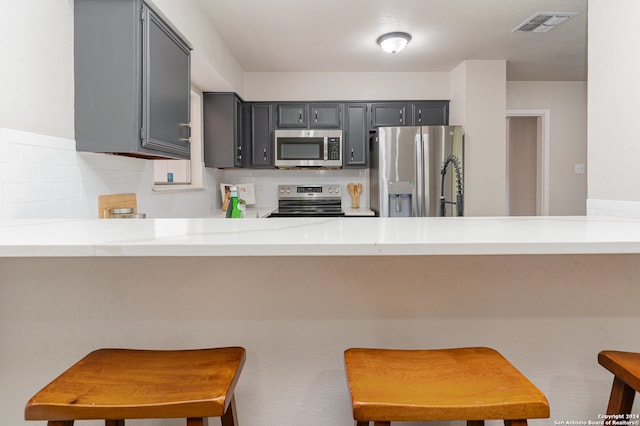 kitchen featuring kitchen peninsula, appliances with stainless steel finishes, decorative backsplash, a kitchen breakfast bar, and gray cabinets