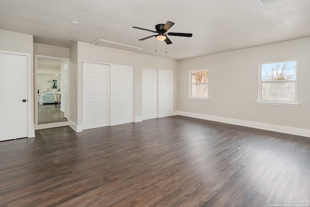 unfurnished bedroom featuring dark hardwood / wood-style floors, ceiling fan, and multiple closets