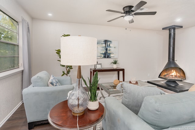 living room featuring a wood stove, ceiling fan, and dark wood-type flooring