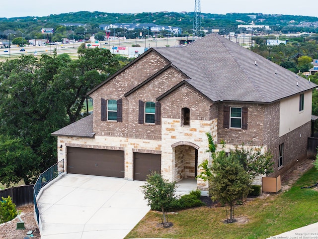 french country inspired facade with an attached garage, brick siding, a shingled roof, driveway, and stone siding