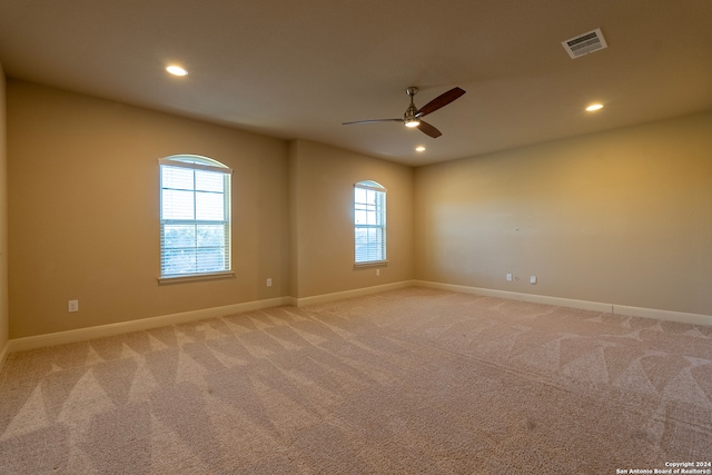 empty room with a wealth of natural light, ceiling fan, and light colored carpet