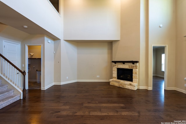 unfurnished living room with a stone fireplace, dark hardwood / wood-style flooring, and a towering ceiling