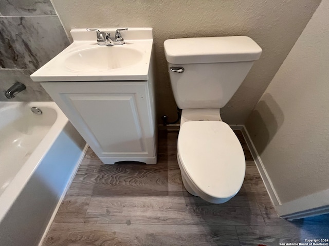 bathroom with hardwood / wood-style floors, vanity, a bath, and toilet