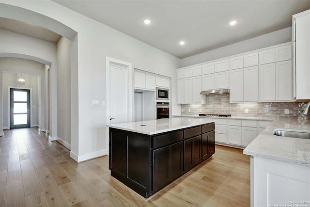 kitchen with sink, backsplash, a center island, white cabinets, and stainless steel oven