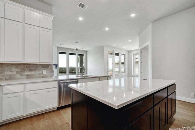 kitchen with sink, a center island, white cabinets, stainless steel dishwasher, and light wood-type flooring