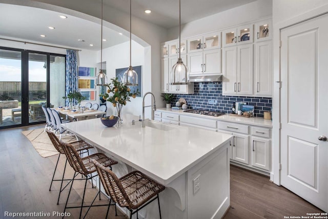 kitchen with sink, stainless steel gas stovetop, a kitchen island with sink, decorative backsplash, and white cabinets