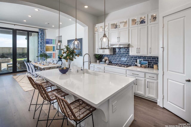 kitchen featuring tasteful backsplash, an island with sink, sink, white cabinets, and stainless steel gas cooktop