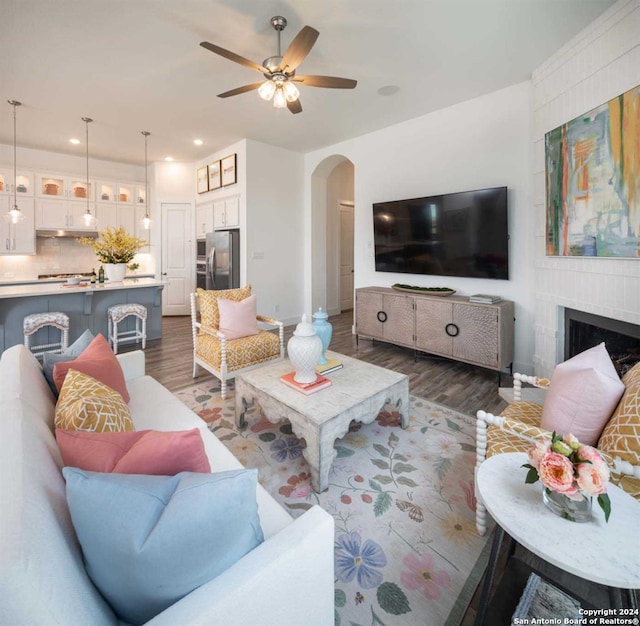 living room featuring a brick fireplace, dark wood-type flooring, and ceiling fan