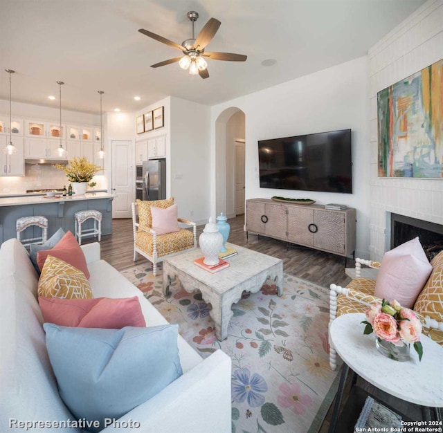 living room featuring a fireplace, dark wood-type flooring, and ceiling fan