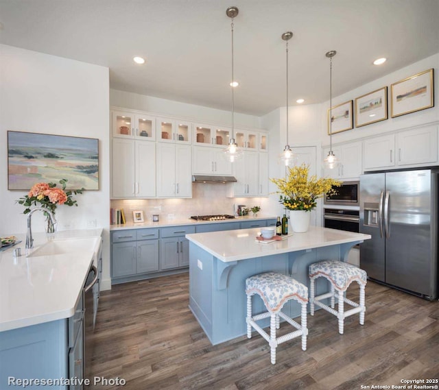 kitchen featuring sink, appliances with stainless steel finishes, white cabinetry, a kitchen bar, and decorative light fixtures