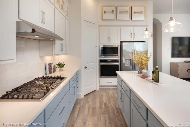 kitchen with appliances with stainless steel finishes, pendant lighting, white cabinetry, decorative backsplash, and light hardwood / wood-style floors