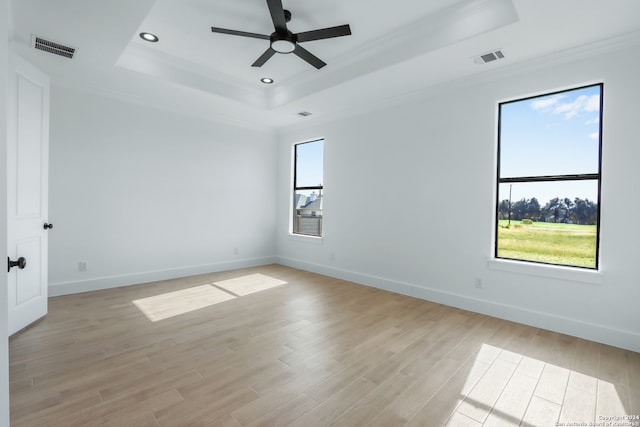 empty room with a tray ceiling, crown molding, light hardwood / wood-style flooring, and a healthy amount of sunlight