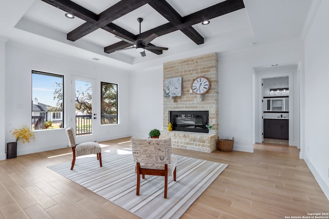 living room featuring ceiling fan, light hardwood / wood-style floors, coffered ceiling, and a brick fireplace