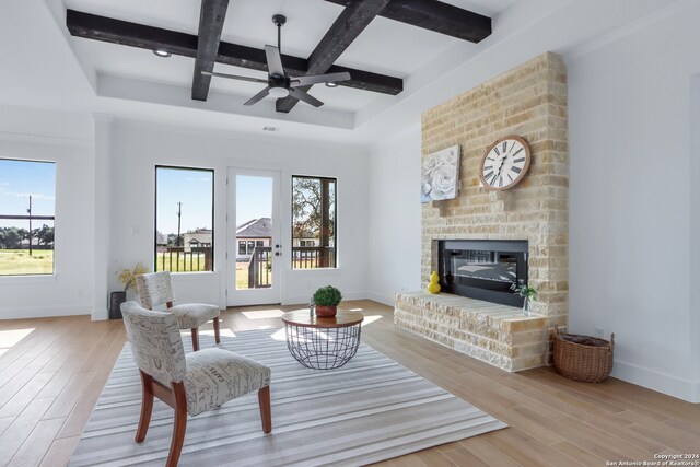 living room with beam ceiling, ceiling fan, coffered ceiling, a fireplace, and light wood-type flooring