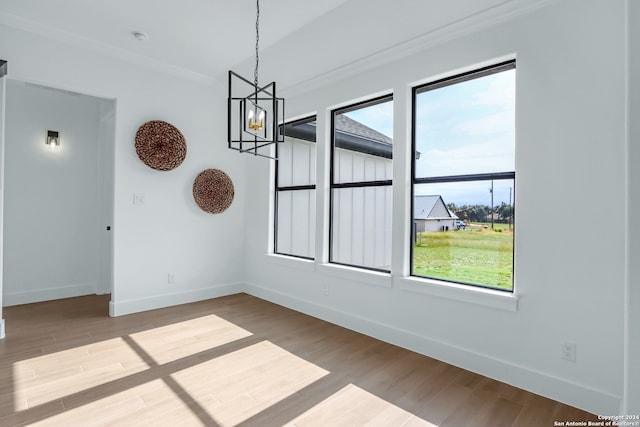 unfurnished room featuring wood-type flooring, an inviting chandelier, plenty of natural light, and ornamental molding