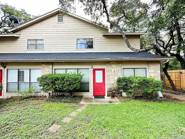 townhome / multi-family property featuring fence, a shingled roof, a front yard, and stone siding