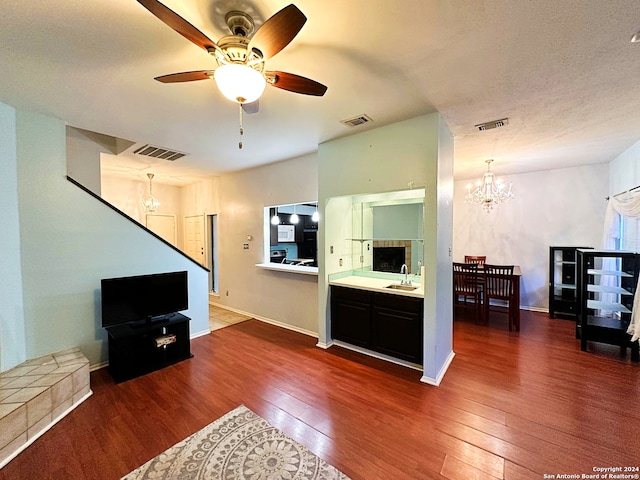 living room with a textured ceiling, ceiling fan with notable chandelier, dark wood-type flooring, and sink