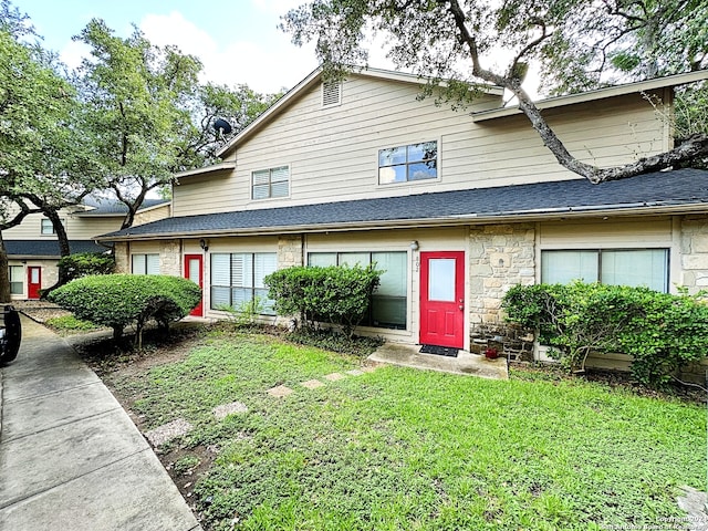 multi unit property featuring roof with shingles, a front yard, and stone siding