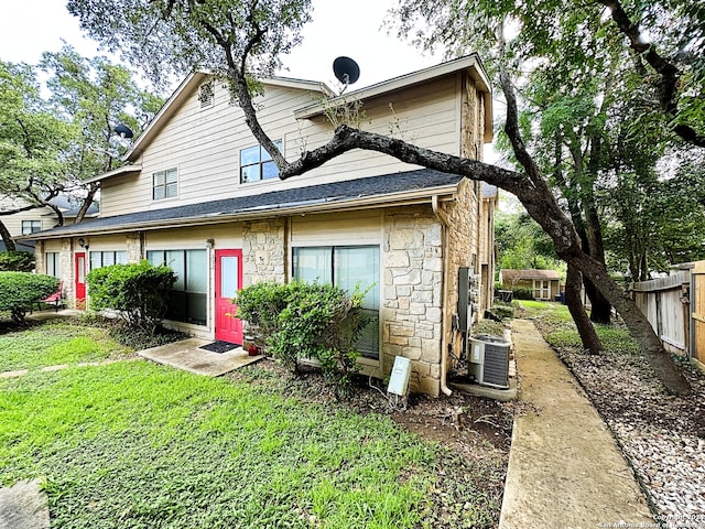 back of house with stone siding, a shingled roof, a lawn, fence, and central AC