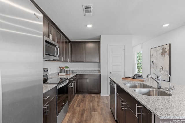 kitchen with dark wood-type flooring, sink, light stone countertops, appliances with stainless steel finishes, and dark brown cabinetry