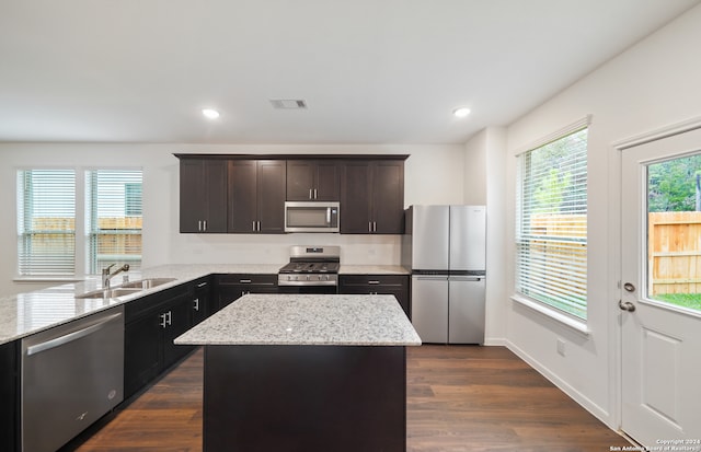 kitchen featuring sink, dark wood-type flooring, stainless steel appliances, light stone counters, and a kitchen island