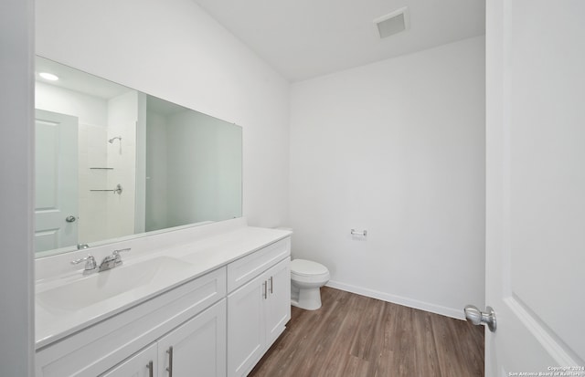 bathroom with hardwood / wood-style floors, vanity, toilet, and walk in shower