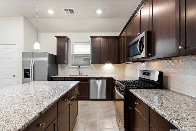 kitchen with sink, appliances with stainless steel finishes, hanging light fixtures, dark brown cabinets, and light stone countertops