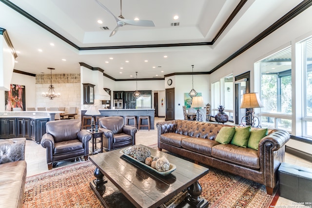 living room featuring ceiling fan with notable chandelier, ornamental molding, and a tray ceiling