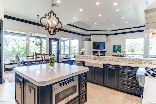 kitchen featuring stainless steel microwave, sink, a center island, an inviting chandelier, and decorative light fixtures